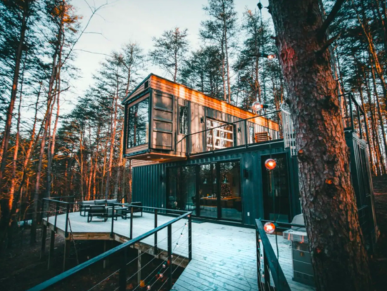 cabin made of three shipping containers stacked on each other in woods in winter