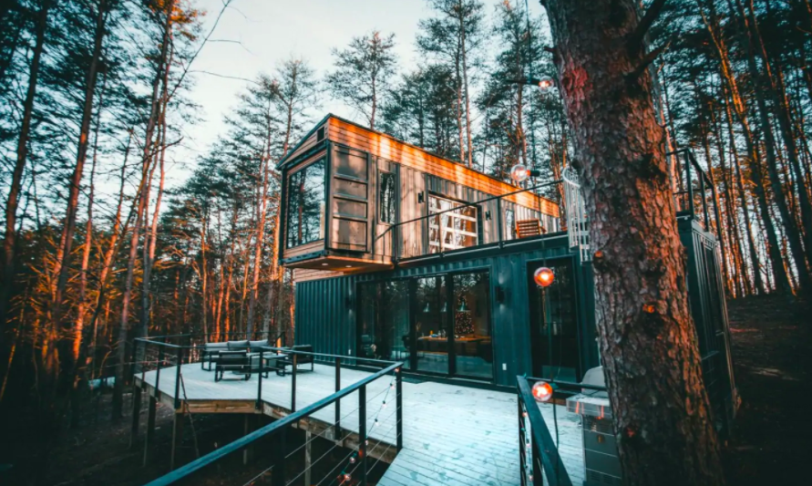 cabin made of three shipping containers stacked on each other in woods in winter