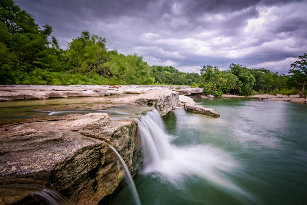 short waterfall into dark teal lake day trips from Austin