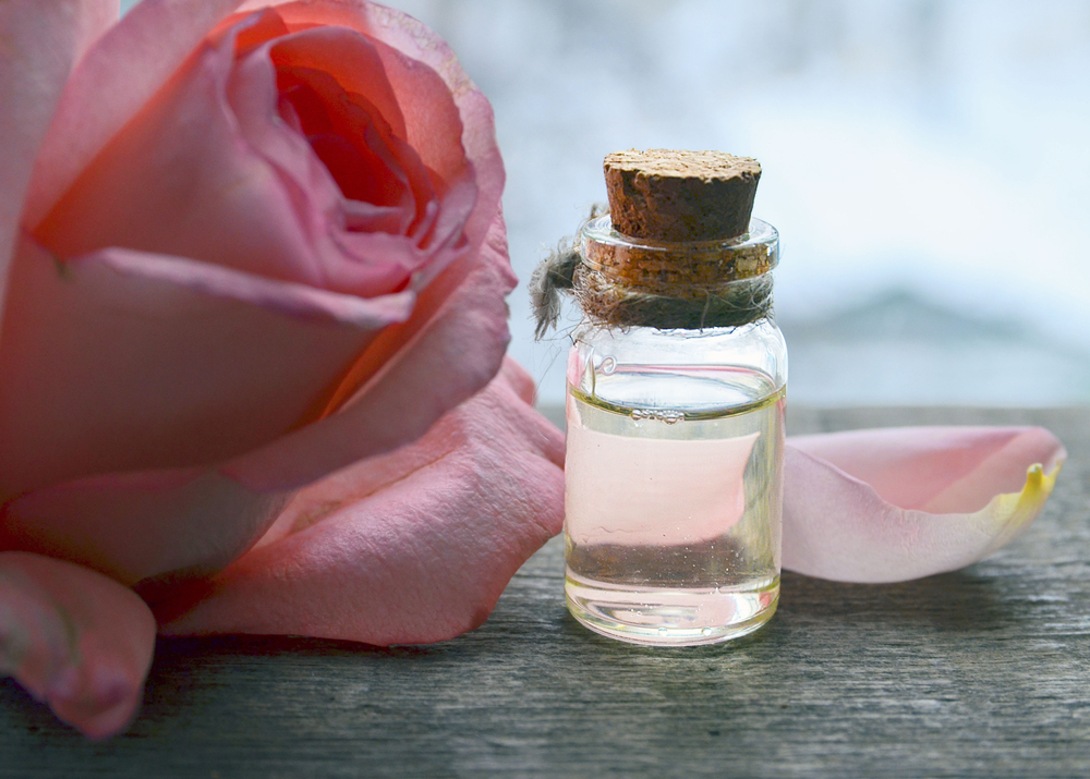 a bottle on a table with a pink rose 