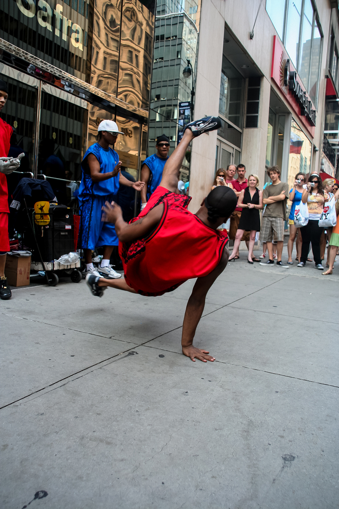 A person on the street break dancing surrounded by a crowd,