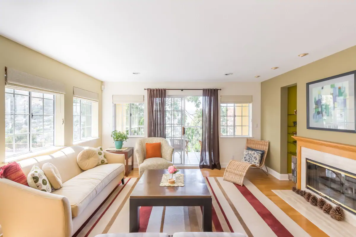 Spacious and tasteful living room with a rug, couch, fireplace, and surrounding windows.  San Francisco Airbnb.