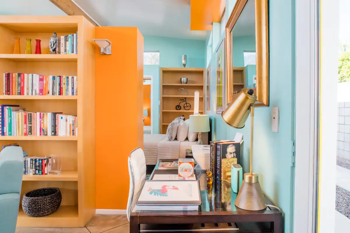 GORGEOUS interior of Dream House, best Airbnb in Palm Springs, California... the living room and study area, with book shelves, a desk, and lovely creamsicle-orange and turquoise walls.