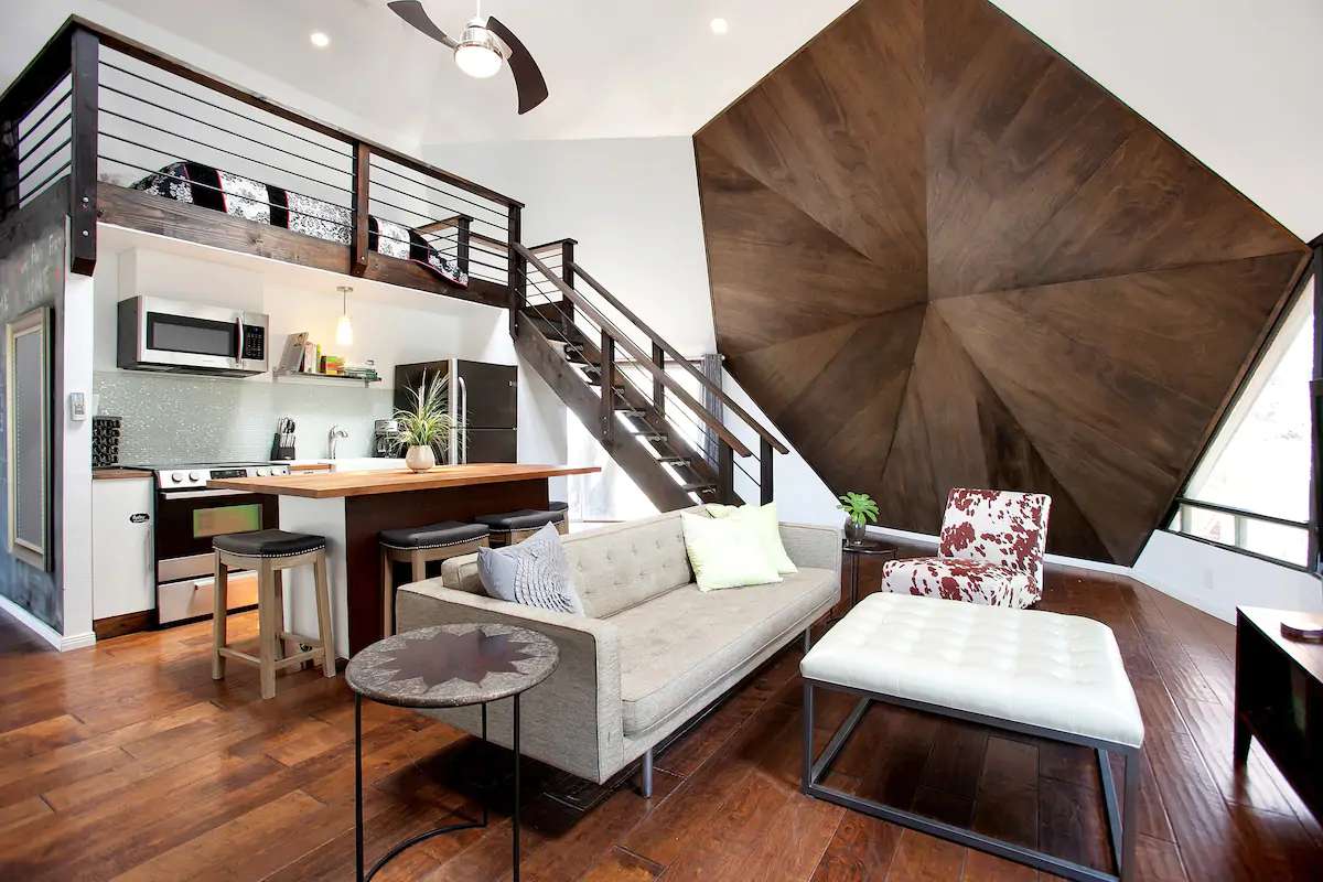 A cozy, wood-accented living room, kitchen, and loft bedroom, in a Dome Airbnb in California