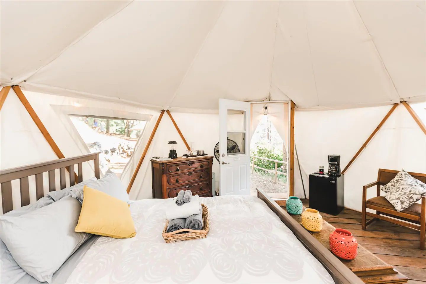 The dreamy, white interior of this small and cozy yurt Airbnb, with a bed, dresser, small fridge, coffee maker, and chair.  One of the best California Airbnbs!
