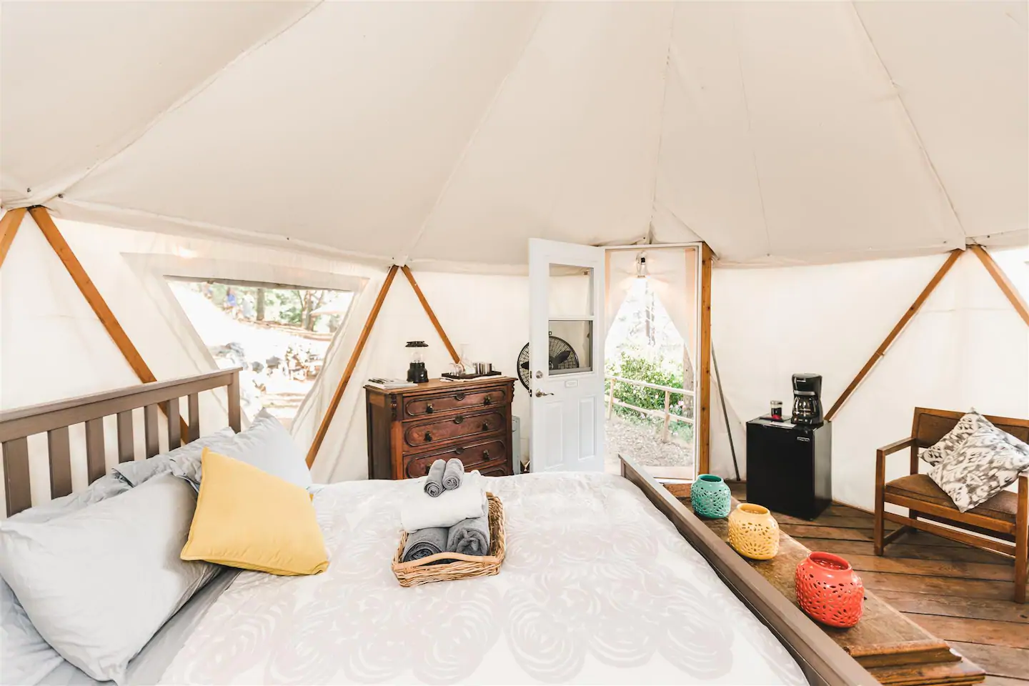 The dreamy, white interior of this small and cozy yurt Airbnb, with a bed, dresser, small fridge, coffee maker, and chair. One of the best California Airbnbs!
