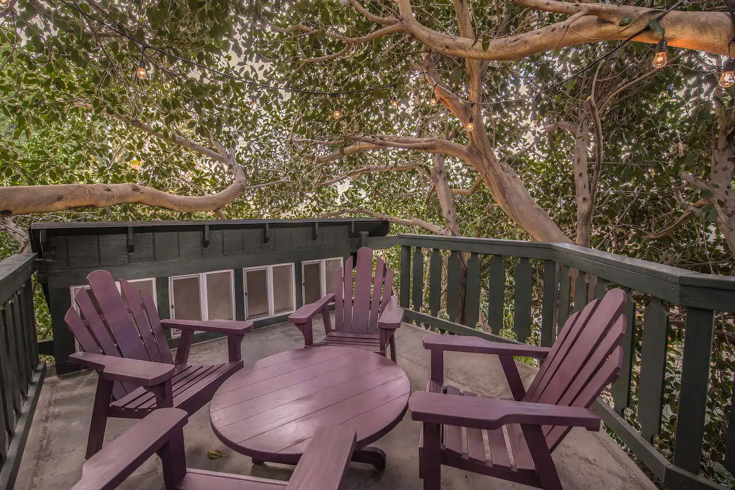 Awesome treehouse deck with outdoor table and chairs, decorated with bulb lights strung overhead.  At the terrific Treehouse Adventure Airbnb in California!
