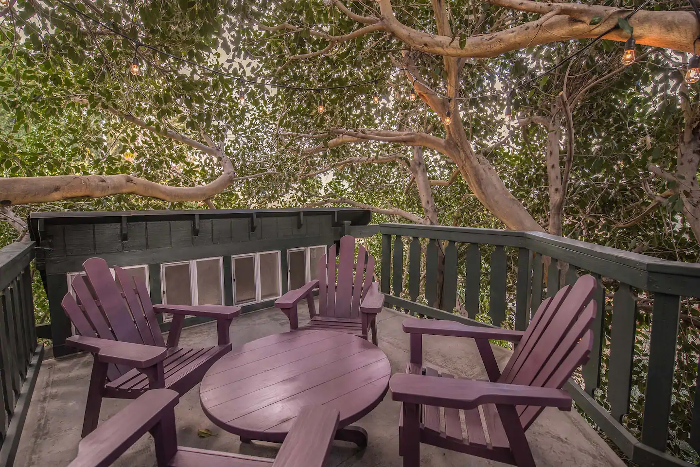 Awesome treehouse deck with outdoor table and chairs, decorated with bulb lights strung overhead. At the terrific Treehouse Adventure Airbnb in California!