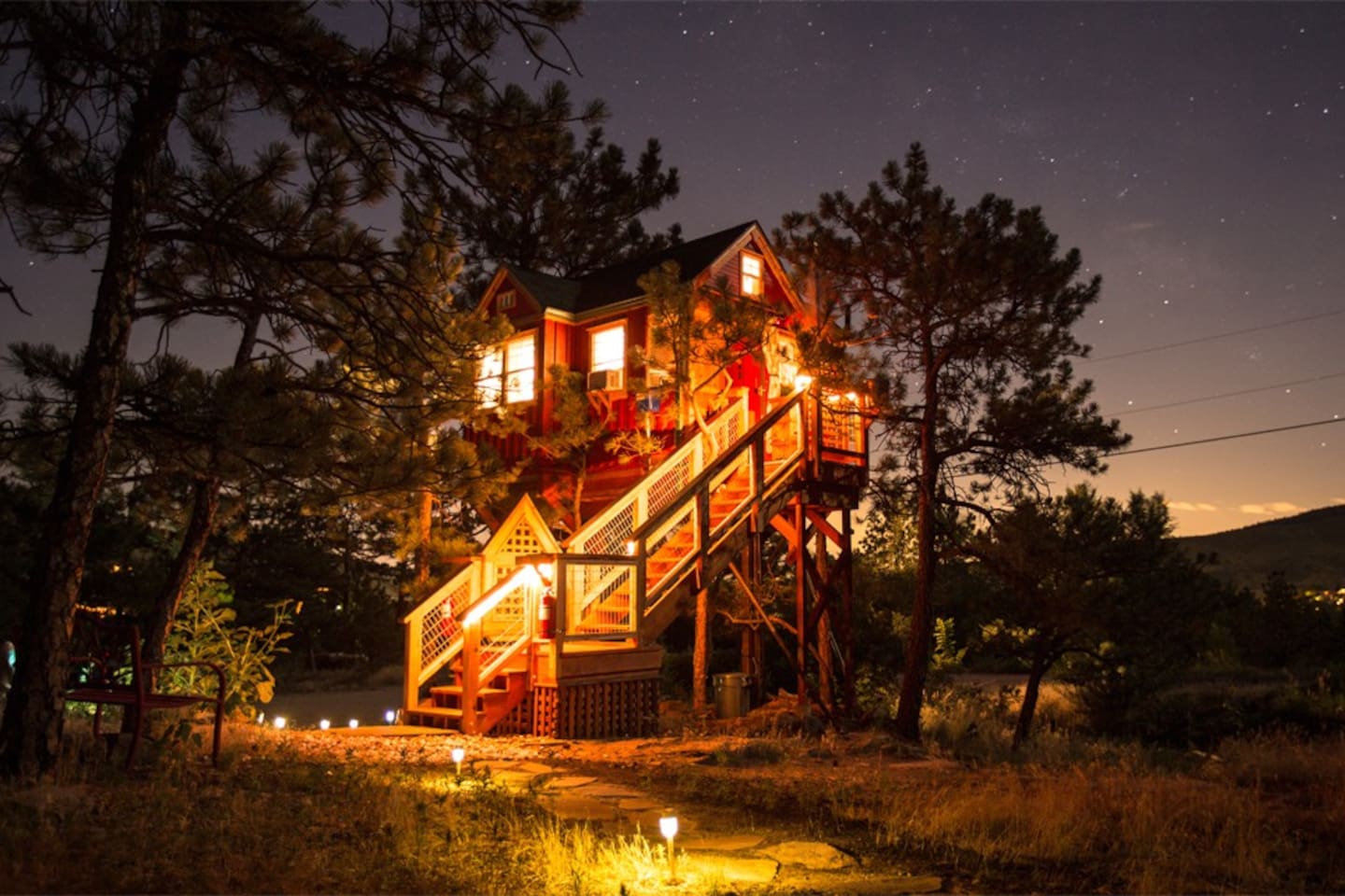 The Little Red Treehouse illuminated at night with lots of stars visible in the sky. This is one of the best Airbnbs in Boulder