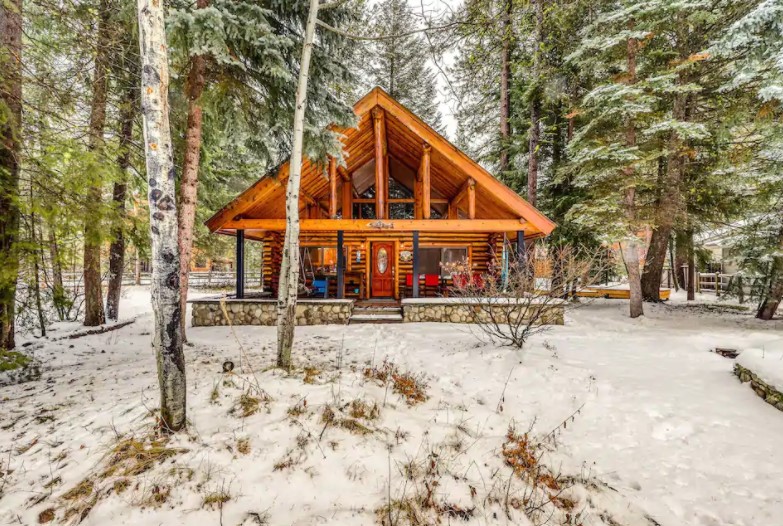 Front view of a traditional log cabin surrounded by tall pines with a light dusting of snow one of the best cabins in Idaho