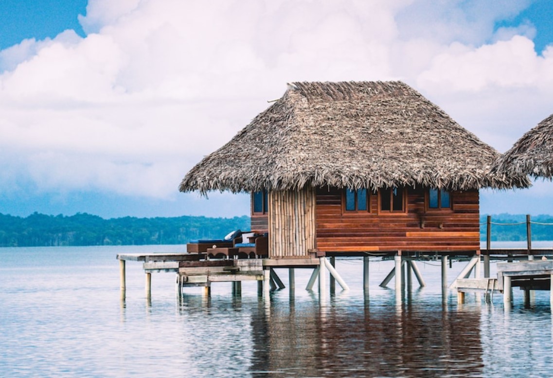 A thatched roof bungalow standing in beautiful water with its own private deck with hills in the far distance