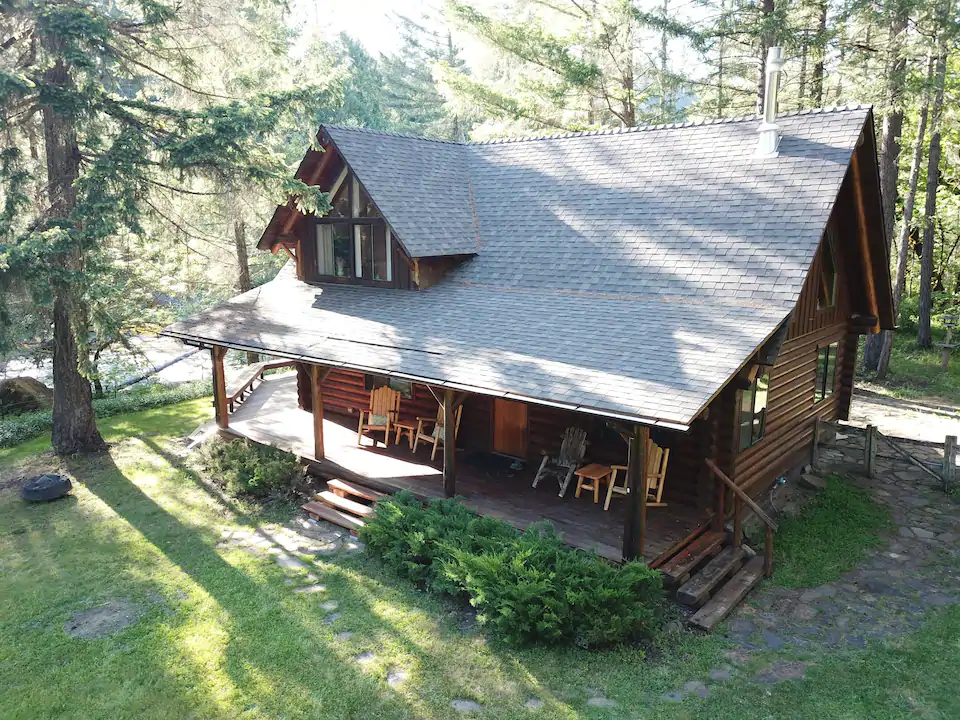 Exterior photo of the Riverfront Forested Cabin, one of the best cabins in Oregon. The surrounding forest and river are both included in the photo, as well as the cabin's comfortable looking front porch. 