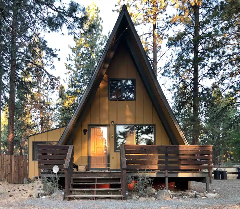 Photo of the A frame of mind cabin from the outside. The cabin is painted a dark mustard yellow and surrounded by pine trees. This is one of the best cabins in Oregon. 