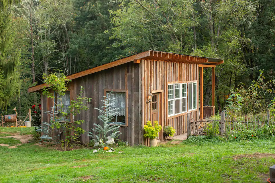 Exterior picture of the Wilson Farm Cottage, one of the best cabins in Oregon. The cabin is small and wood paneled with a lovely garden out front and a charming wooden fence. 