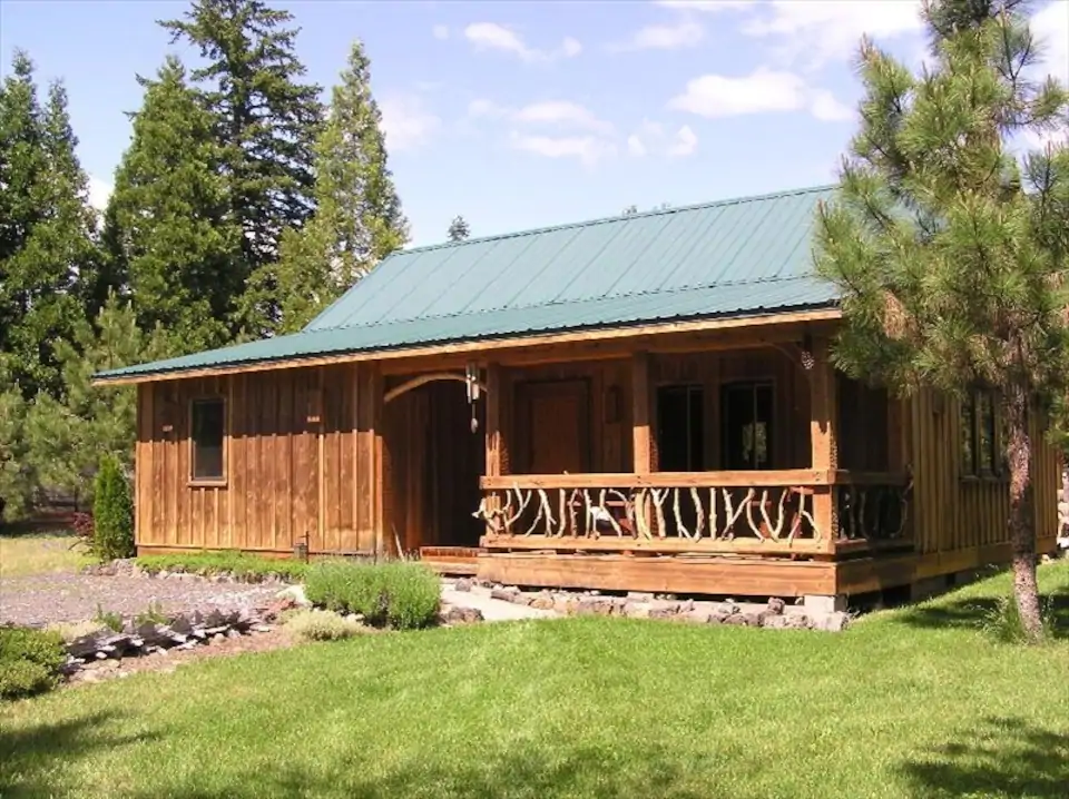 The exterior of the Red Blanket Cabin, one of the best cabins in Oregon. It has a traditional log cabin look and a green tin style roof.