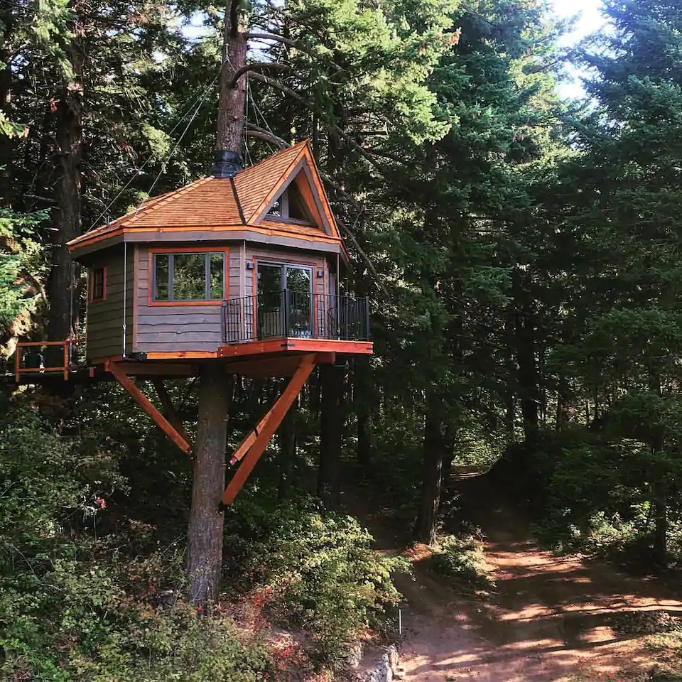 Exterior photo of the Osprey Treehouse, one of the best cabins in Oregon. This shows the octagonal treehouse, the lovely balcony, and the strong pine that supports it. 