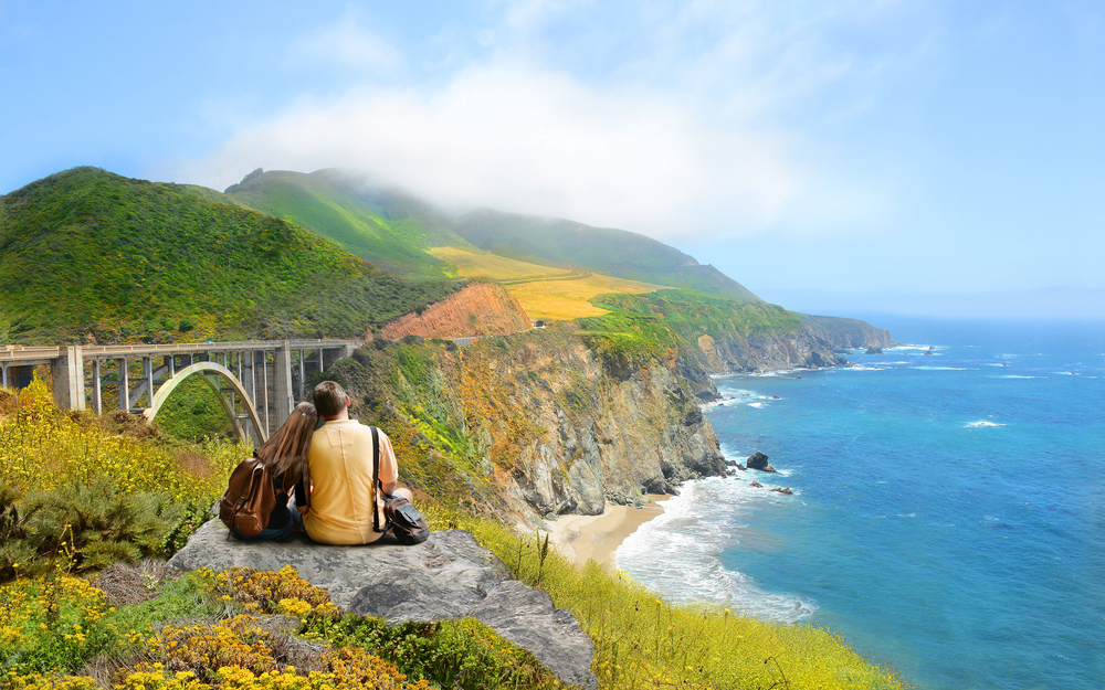 A couple sitting at the edge of a cliff looking out onto the pacific ocean and Big Sur