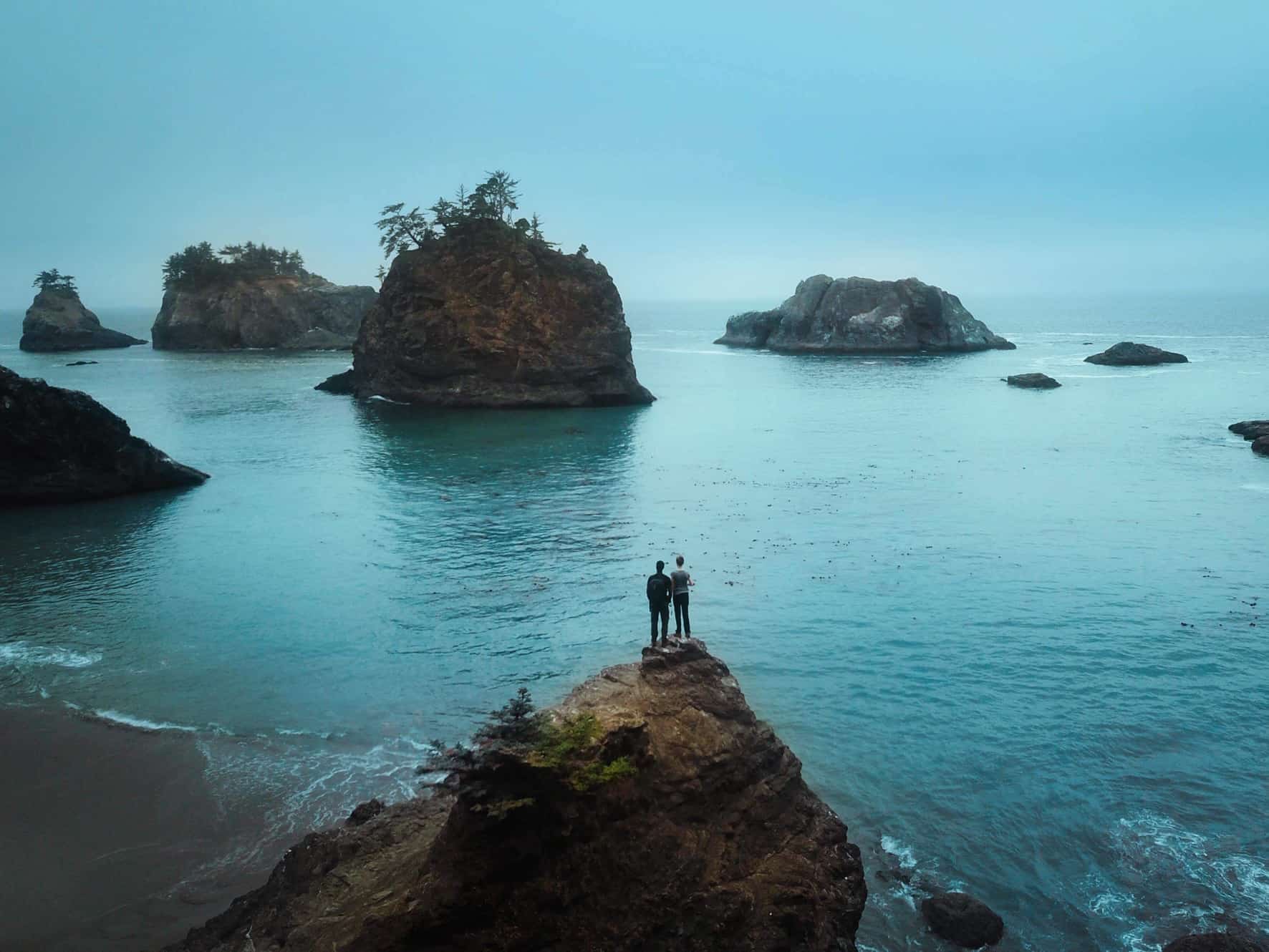 Couple standing on a rock at secret beach in Oregon one of the best honeymoons in the usa