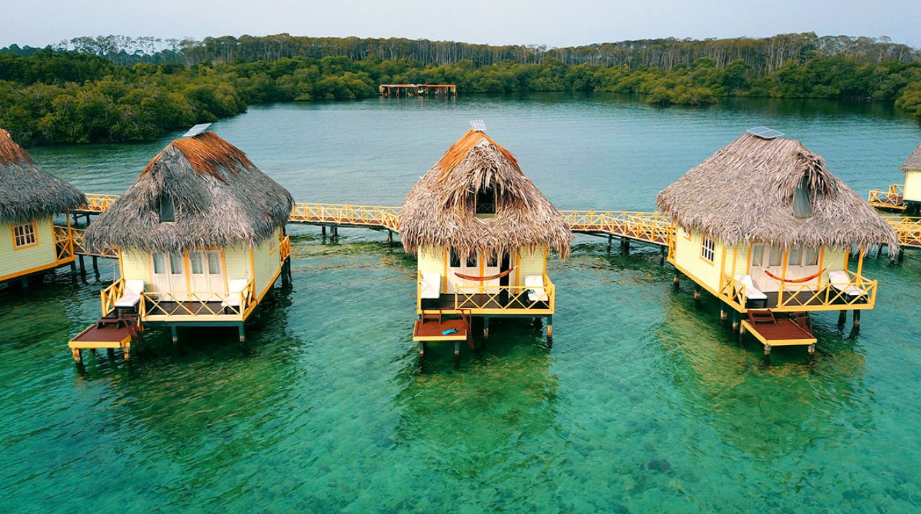 An arial view of several overwater bungalows in a line perched in crystal blue water in Panama