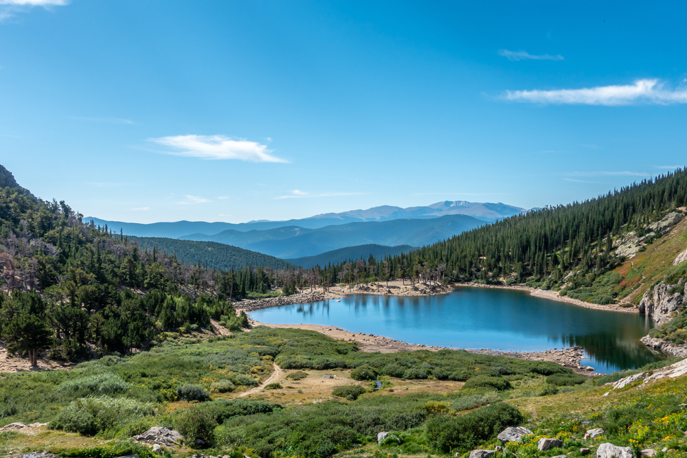 The lake at the bottom of Saint Mary's Glacier surrounded by tall pines and looking out onto mountain ranges