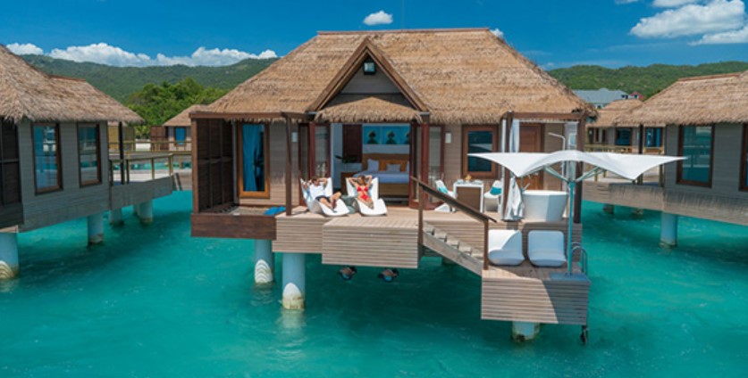 A couple sitting on the private deck of their luxury overwater bungalow at the Sandals Resort in Jamaica