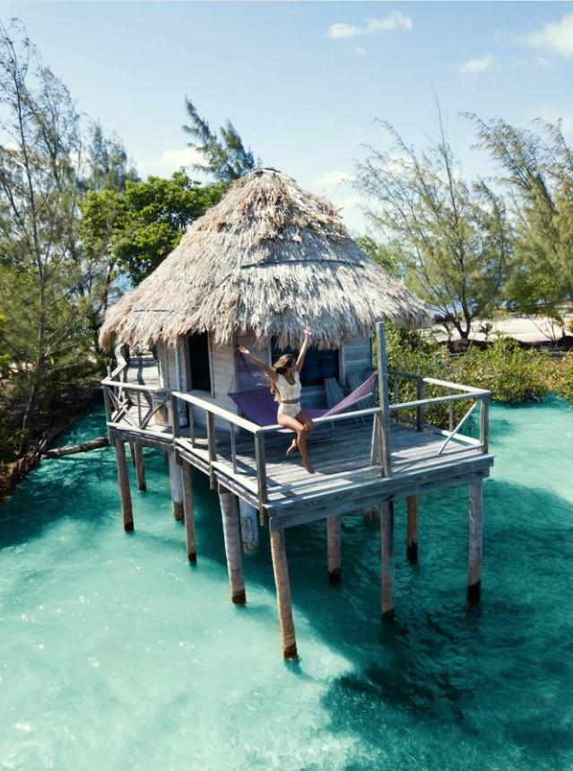 A woman sitting on the railing of a deck of a private overwater bungalow on a private island in Belize