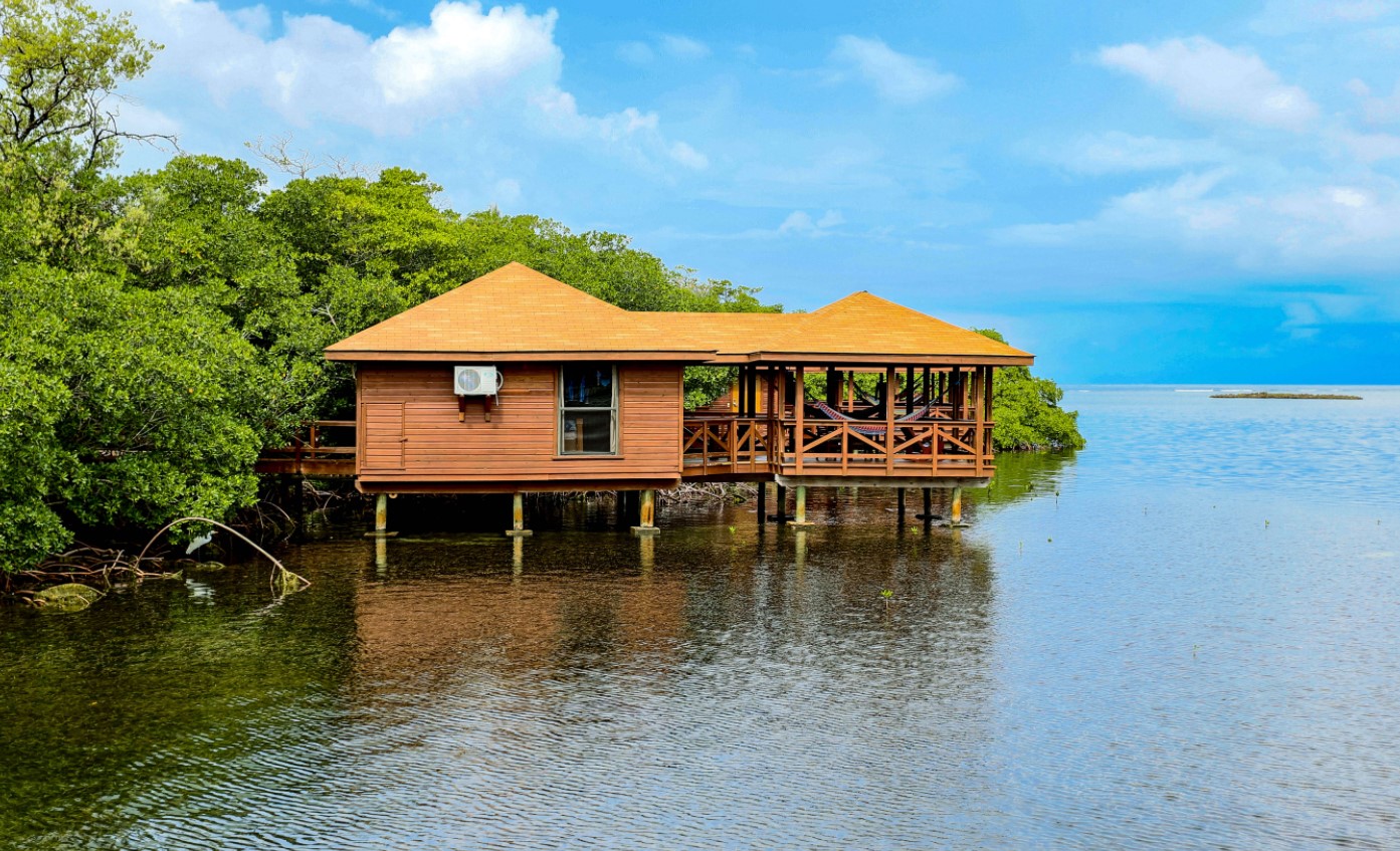 A tan overwater bungalow with a private covered deck with a hammock perched over the ocean in Honduras