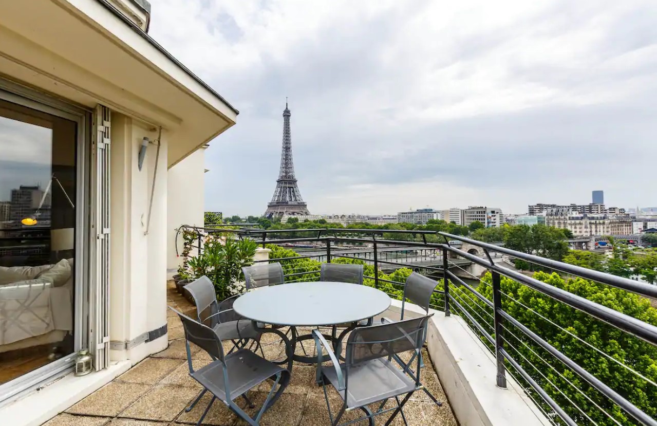 A large balcony with a glass table ad a view of the Eiffel Tower