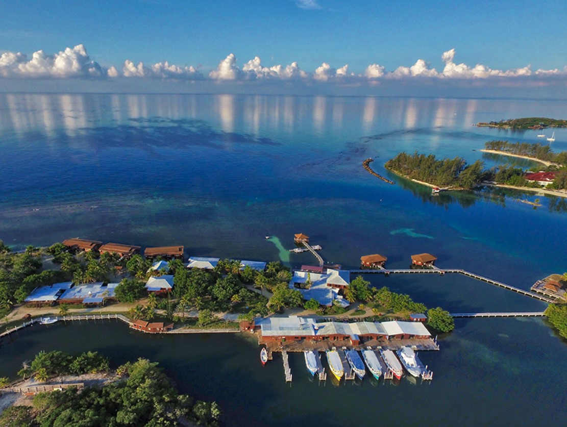 An aerial image of the CoCo View Resort in Honduras with four overwater bungalows in the Caribbean and several ocean front bungalows