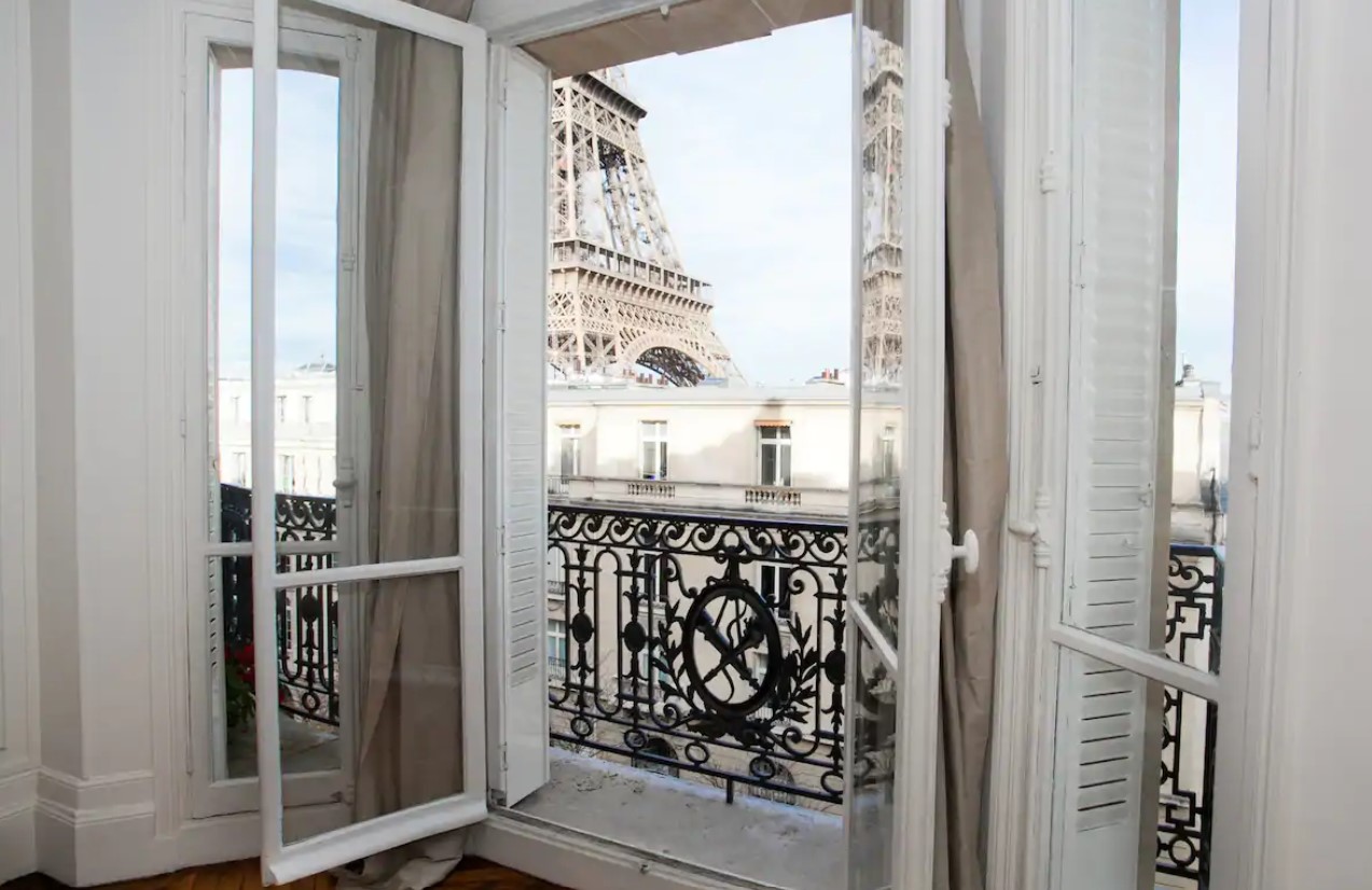 The view of the Eiffel Tower from the open French doors of a charming Paris Airbnb that leads to a private balcony