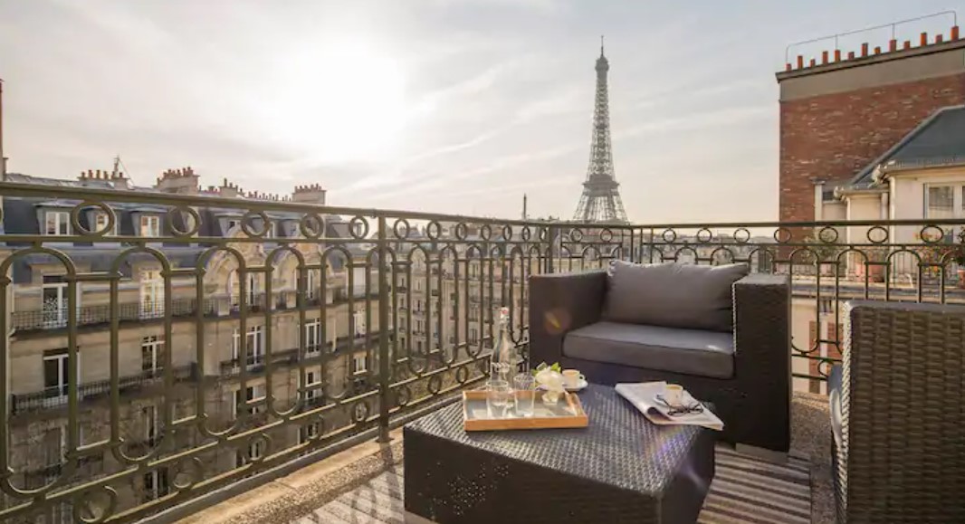 A large balcony with comfy seats and a view of the Eiffel Tower in the background