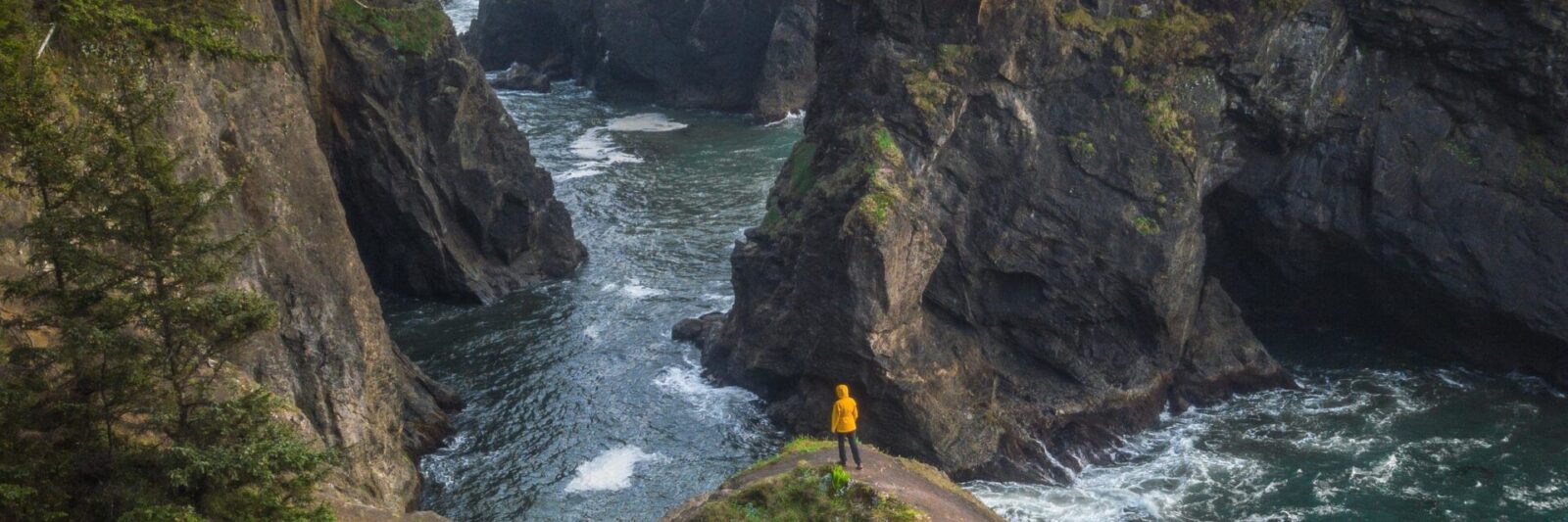 a person hiking in a yellow jacket on a rock bridge on the Oregon Coast