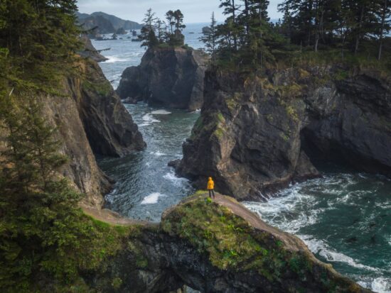 a person hiking in a yellow jacket on a rock bridge on the Oregon Coast