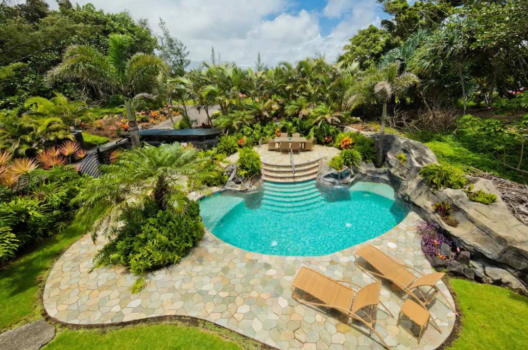 An aerial view of a large in ground pool surrounded by a stone patio and lush tropical greenery best airbnbs in Hawaii