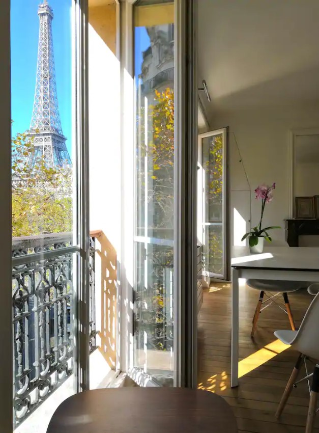 Looking through the side of a balcony door that leads to a small balcony with views of the Eiffel Tower