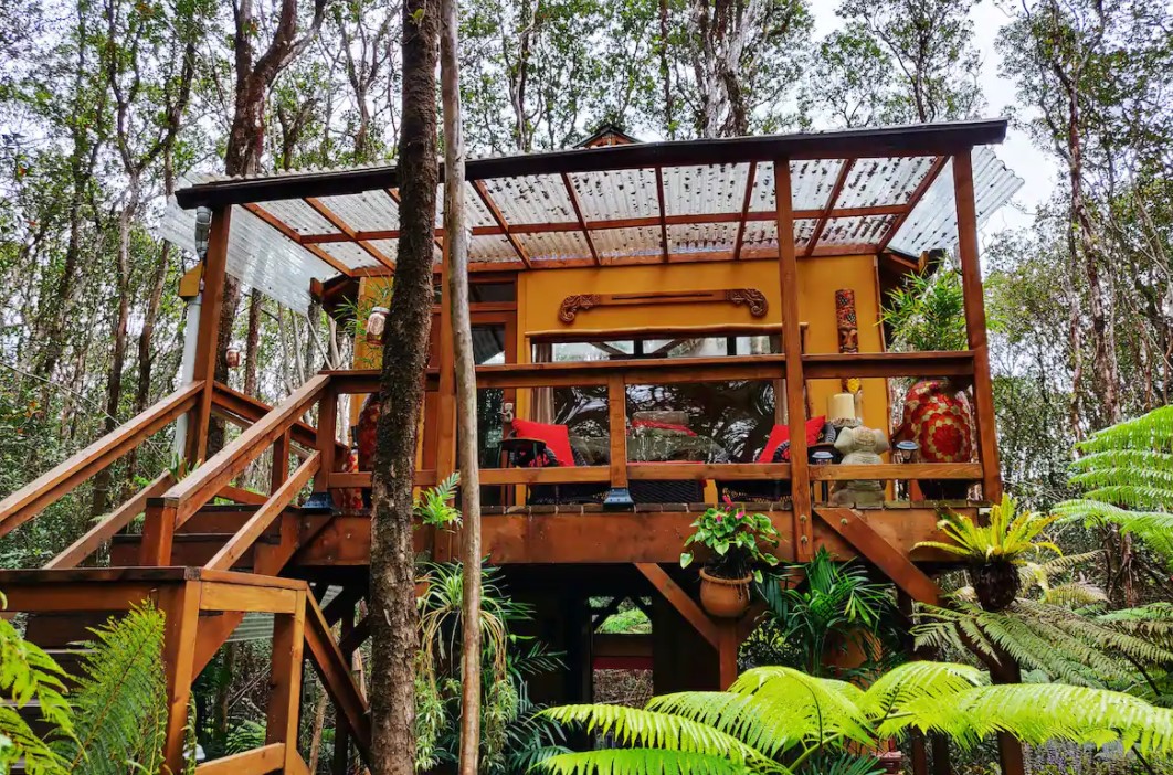 The exterior of a treehouse looking at a second floor lanai with a clear over hang surrounded by lush tropical greenery