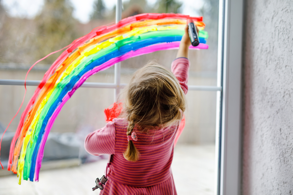 A child drawing a rainbow on a window