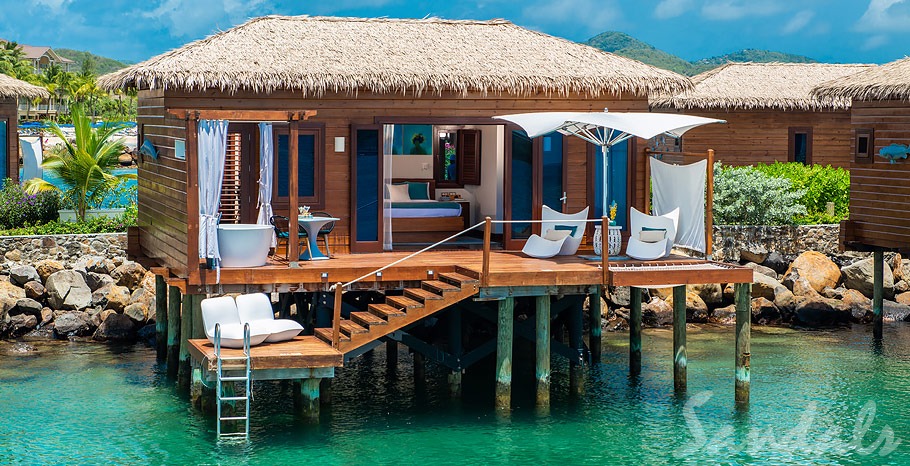 A large overwater bungalow with a private deck that has a large tub, sun loungers, a bistro set, and direct access to the ocean