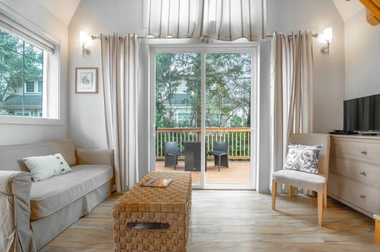 The interior sitting area of a cottage featuring white and beige décor and a large French door that leads to a private deck