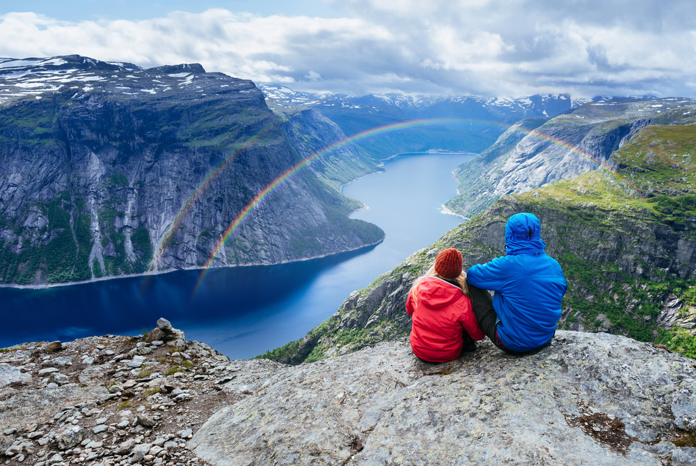 A couple sat at the top of a mountain looking down on a rainbow. Rainbow quotes can be romantic too