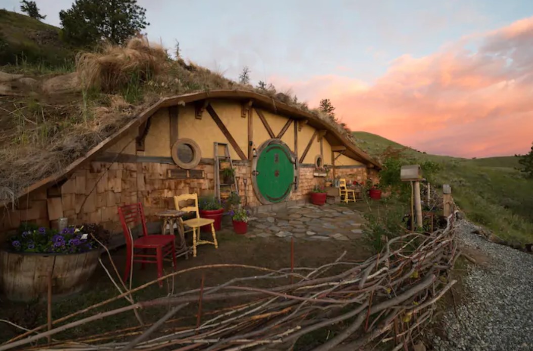 A Hobbit Hole inspired Earth house that is built into the side of a mountain with a pale yellow exterior and a large circular kelly green door best Airbnbs in Washington