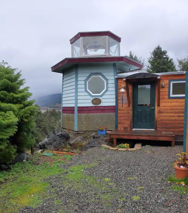 A tiny home on the side of a mountain near the pacific ocean that has part of it shaped like a lighthouse