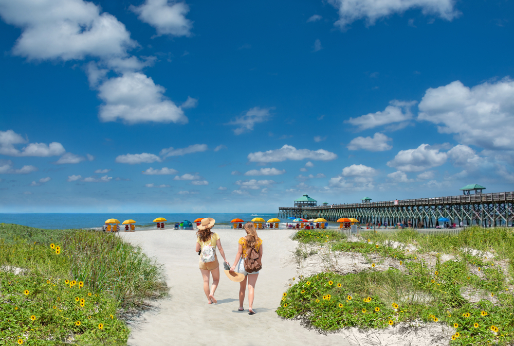 Two people walking towards the beach and pier at Folly Beach South Carolina one of the best beach towns in the usa
