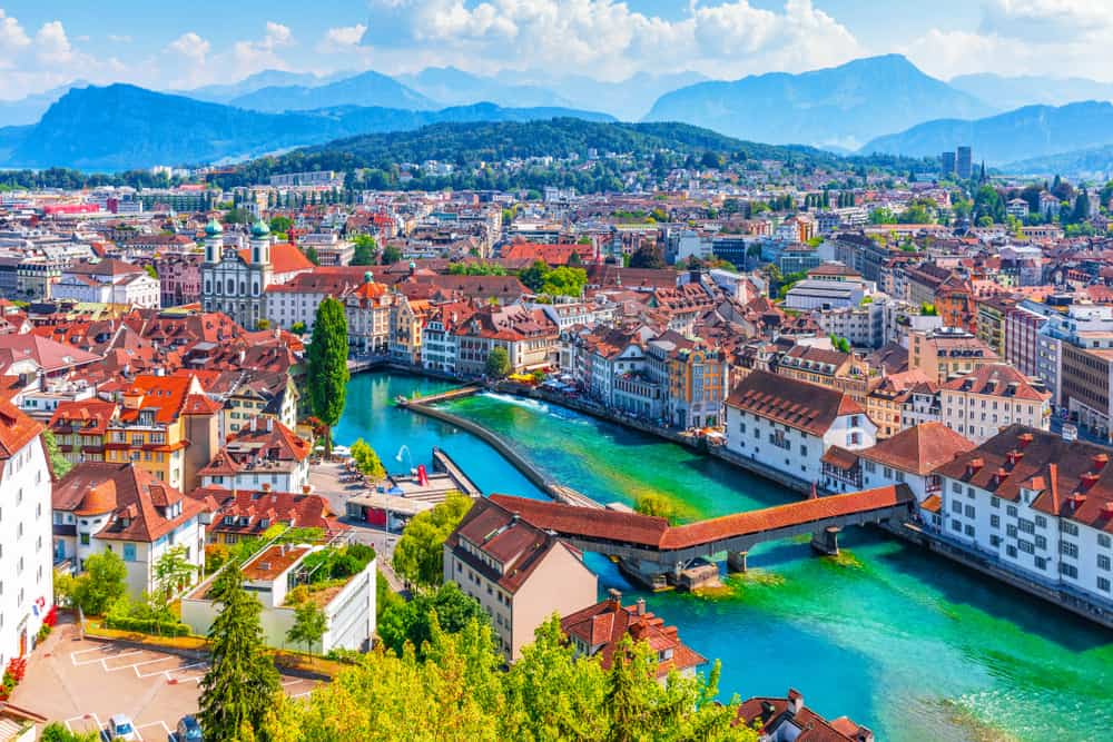 An aerial view of the beautiful Swiss city Lucerne with a river cutting through it and mountains in the distance.