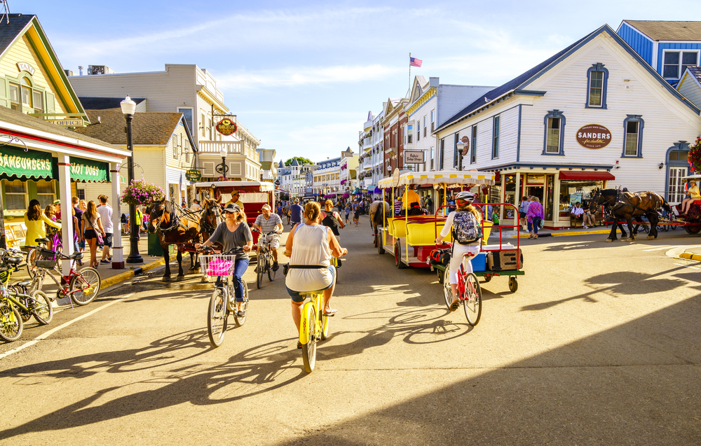 A busy street with people riding bikes, a small trolley, and horse drawn carriages on Mackinac Island in Michigan best small beach towns in the usa