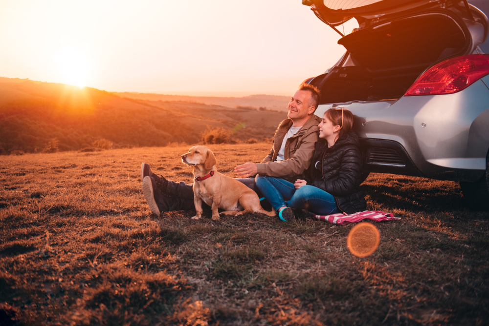 Father and daughter sitting in front of a car on a road trip