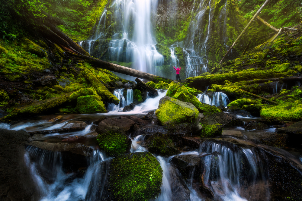 Person in a red jacket standing at the base of Proxy Falls in Oregon USA