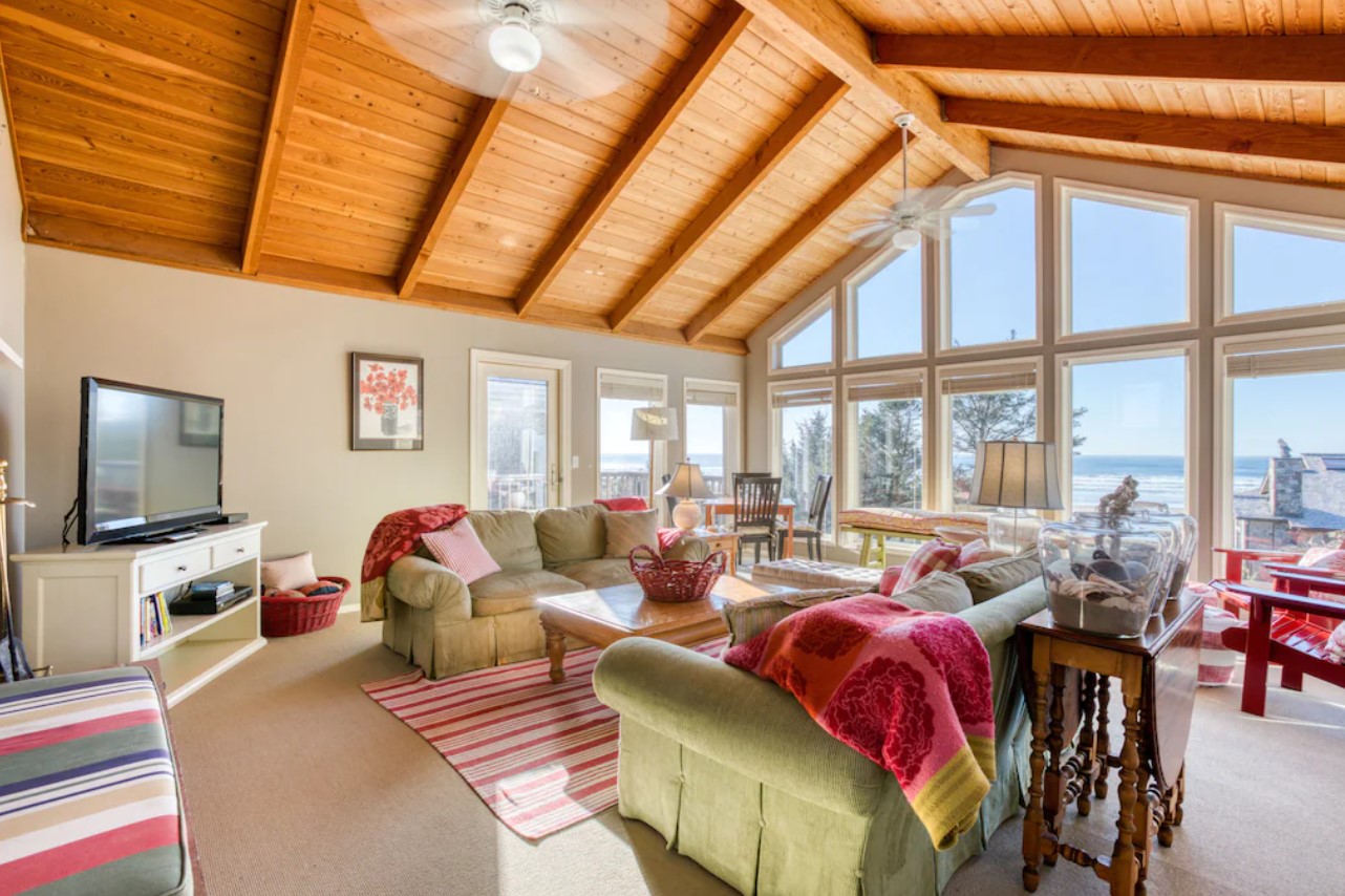 The interior of a large beach house in Oregon with couches, chairs and floor to ceiling windows with views of the ocean