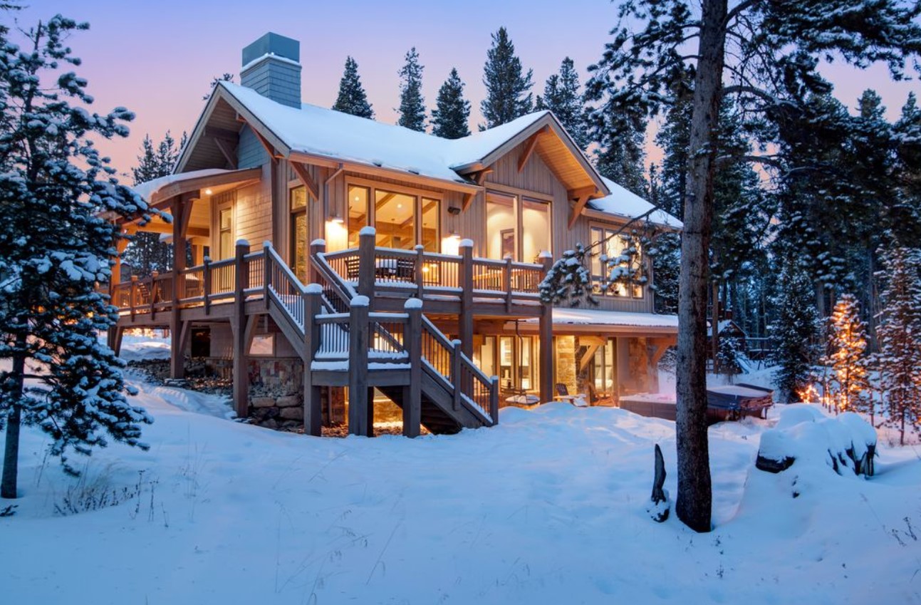 A large luxury villa in the mountains at twilight, covered in snow, and all lit up form the inside. 