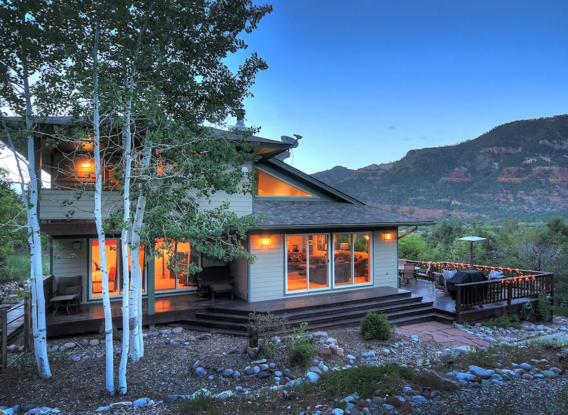 A large mountain home with a modern design with red cliffs in the distance at twilight